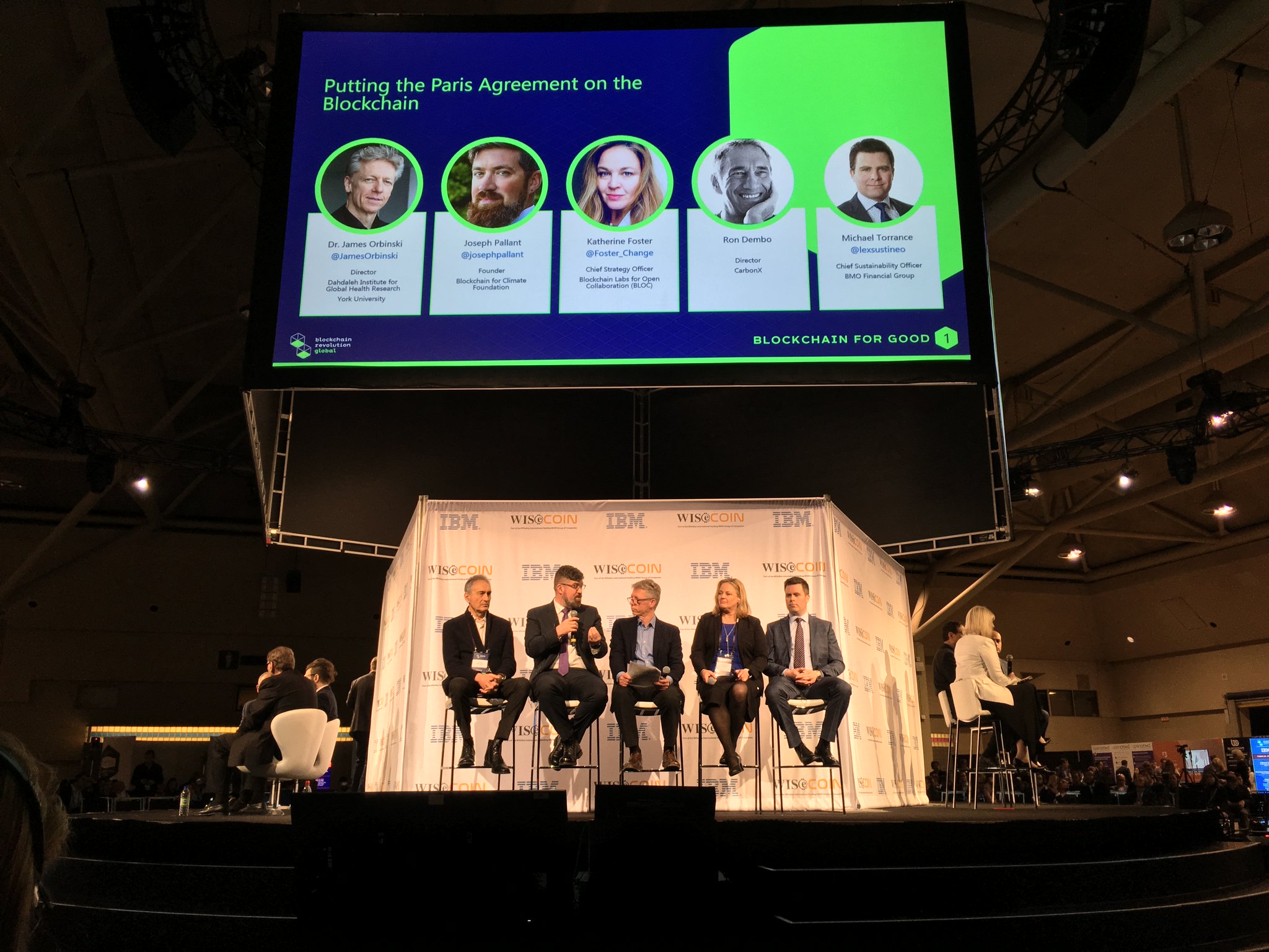 Five people sit in a row on a stage at the Blockchain Revolution Global conference, including Dahdaleh Institute Director James Orbinski and Joseph Pallant