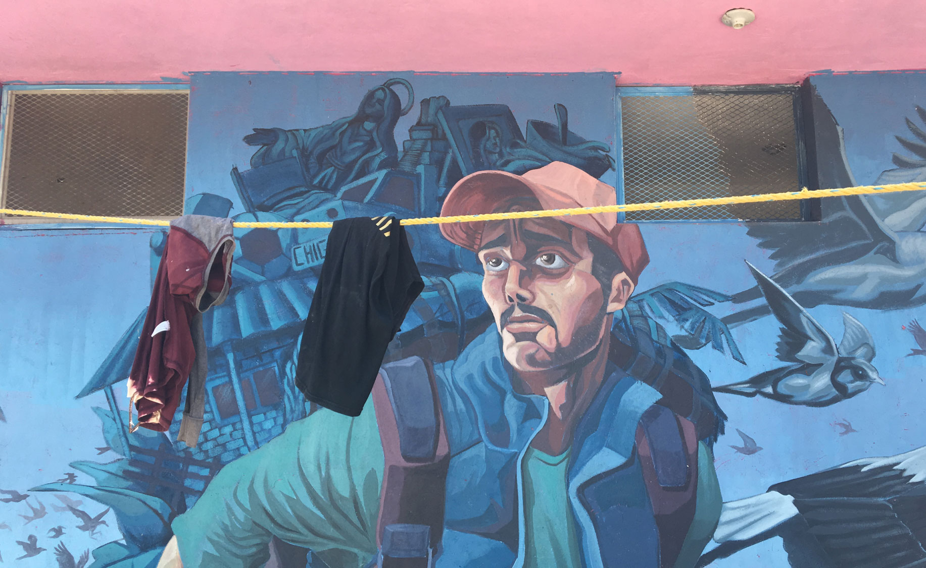 Clothes hang in front of a mural depicting a male migrant