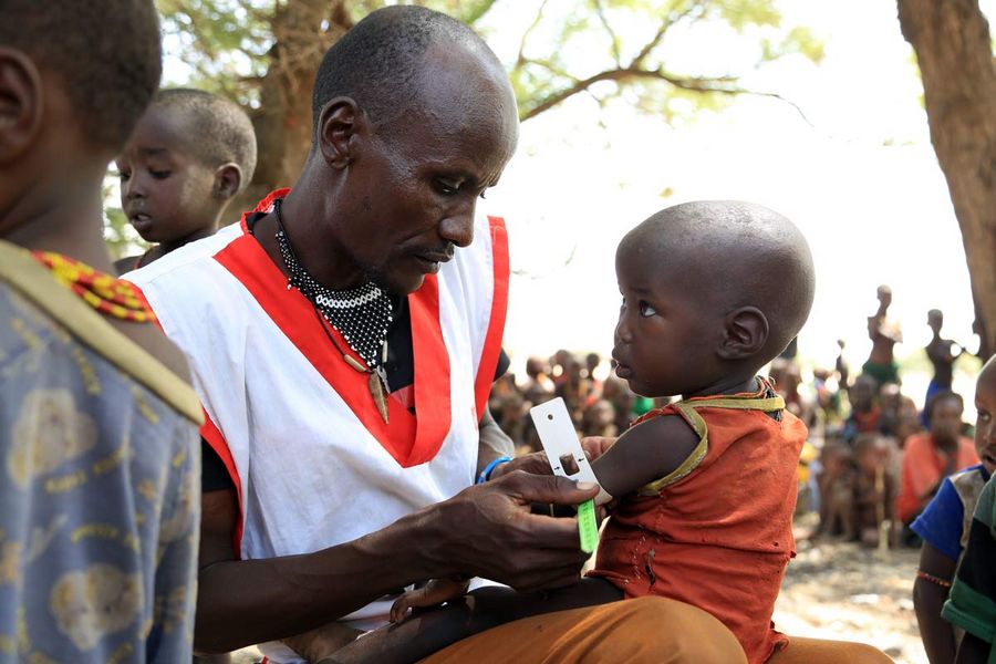 A humanitarian field worker conducts a MUAC test on a young child